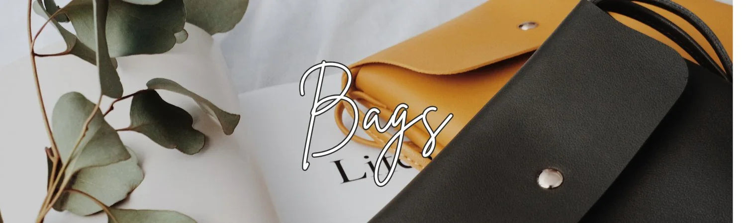 Close-up of mustard yellow and black leather bags with button detail, eucalyptus leaves, and white background